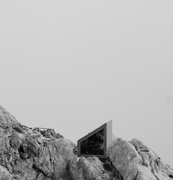 Minimalist mountain shelter placed among rocky terrain under overcast sky.